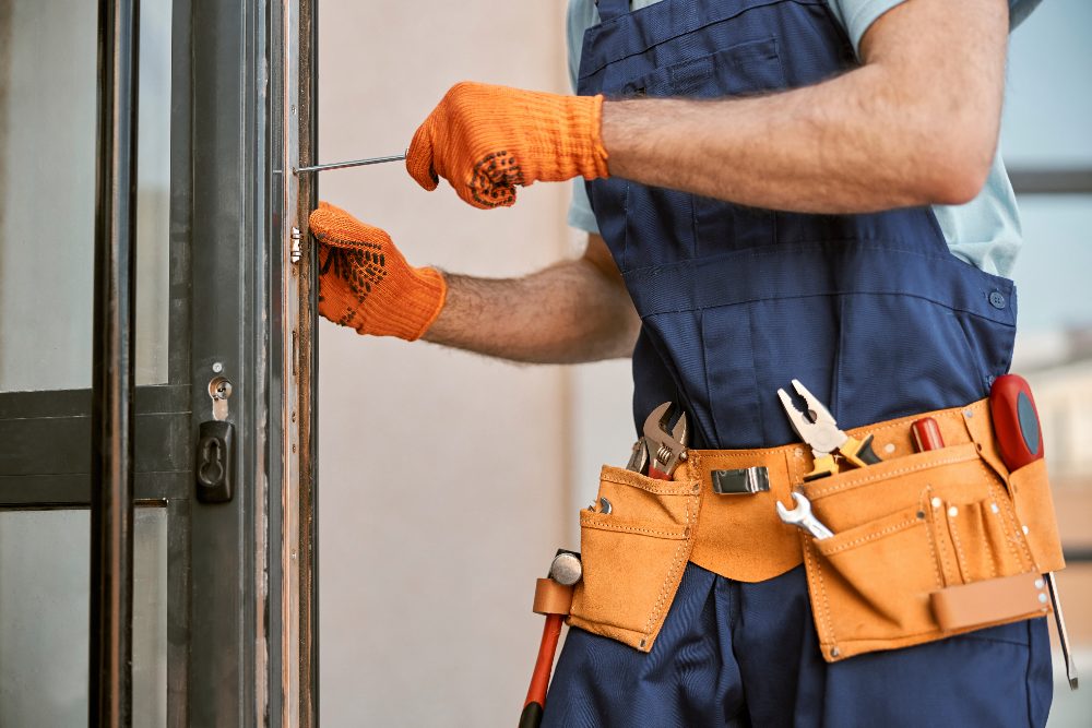 Tradesman in orange gloves and tool belt adjusting door frame with screwdriver